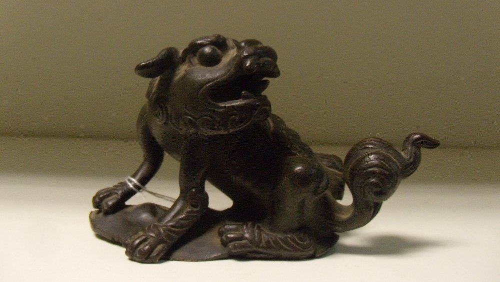 An 18th century bronze Buddhist lion scroll weight,: An 18th century bronze Buddhist lion scroll weight, the animal seated looking towards its tail as it roars, 12cm (4.75 in) wide