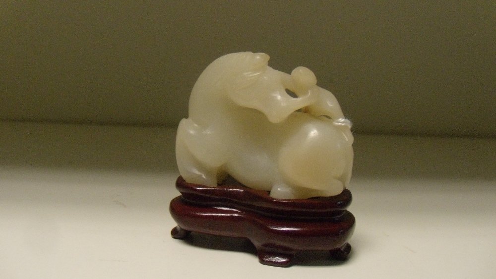 A mutton fat jade group: A mutton fat jade group of a reclining horse nuzzling the figure climbing onto its rump, 4.5cm (1.25 in) wide, with a wood stand (2)