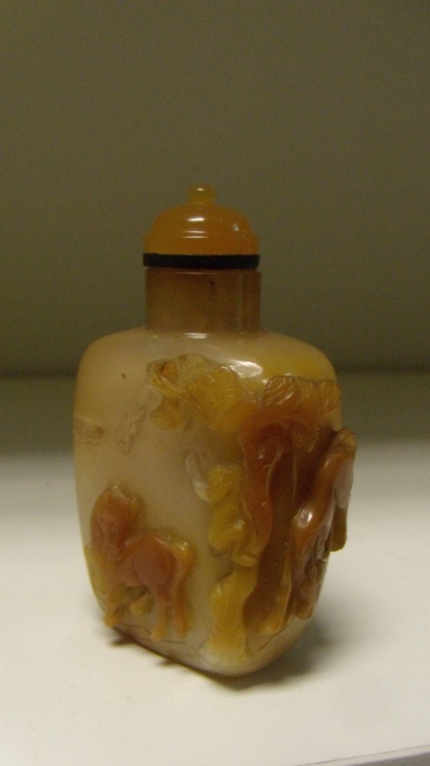 An agate snuff bottle and stopper,: An agate snuff bottle and stopper, the toffee covered inclusions to the mottled grey stone carved with two horses below a monkey climbing a tree to pick its fruit, 6.5cm (2.5 in) high