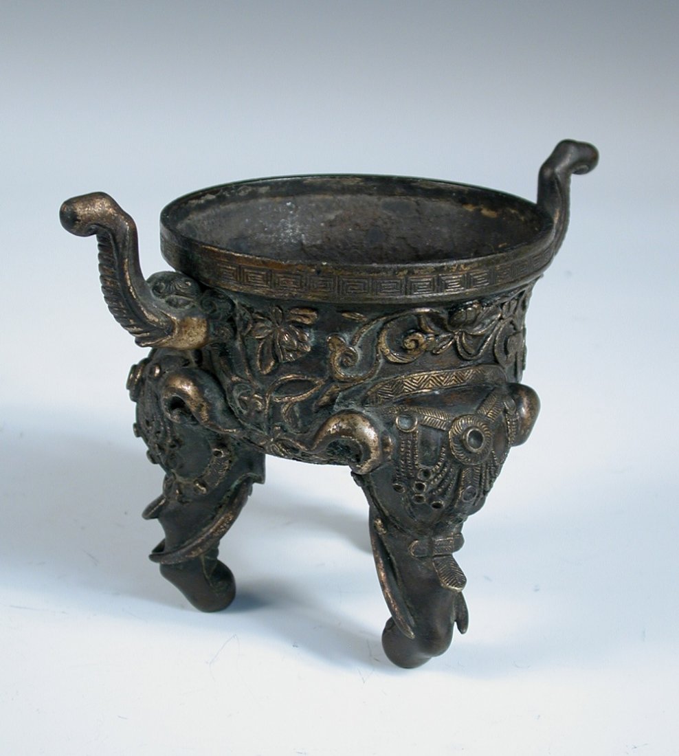 An 18th century parcel gilt bronze incense burner,: An 18th century parcel gilt bronze incense burner, elephant handles applied on a floral band below the thunder scroll rim, the three legs formed of caparisoned elephant heads and their trunks, 10cm (4