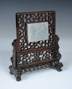 A 19th century nephrite plaque set in hardwood as a: A 19th century nephrite plaque set in hardwood as a table screen the pale green rectangular shape carved in low relief with two horses below a tree, the scroll pierced frame fitting into a stand with