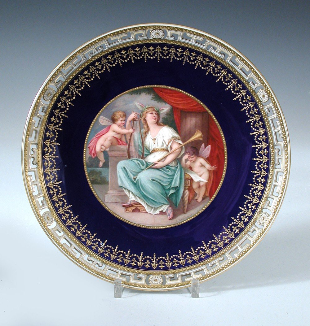 A Minton plate, date code for 1908, painted by Lucien: A Minton plate, date code for 1908, painted by Lucien Boullemier with a classical lady seated below a red drape holding a lyre and a horn, one amorini plucks at the lyre strings and another stands rea
