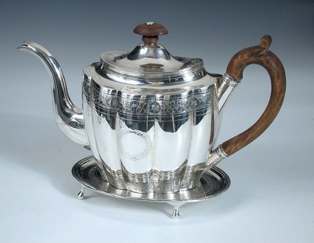 A George III silver matched teapot and stand,: A George III silver matched teapot and stand, the teapot by George Smith (II) & Thomas Hayter, London 1802, oval with lobed body decorated with a band of brightcut engraving, wooden handle and finial,