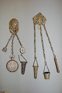 Two pierced gilt metal chatelaines, late 19th cen: Two pierced gilt metal chatelaines, late 19th century, the first cast with a classical warrior's head with thimble bucket, propelling pencil and needle case; the other cast with a palmette suspending