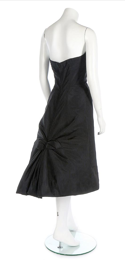 A Jean Dessès couture black faille cocktail dress, late: Description: A Jean Dessès couture black faille cocktail dress, late 1950s, labelled and numbered 6079, the corsetted bodice with pleats forming points to the bodice, the full skirt held in a bow at