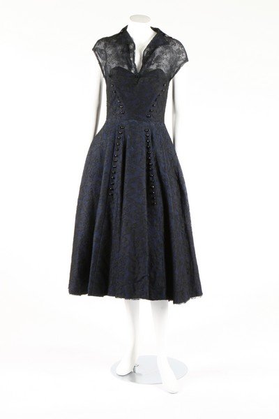 A Jean Desses couture midnight blue lace cocktail: A Jean Desses couture midnight blue lace cocktail dress, 1951. un-labelled, the front closure concealed behind a plastron edged with facetted jet-like buttons, with integral black taffeta corsetted bo