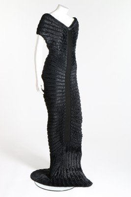 An Azzedine Alaia black chenille-knitted evening gown: An Azzedine Alaia black chenille-knitted evening gown 'Houpette', Spring-Summer, 1994, labelled and size M, the sculpted figure-hugging dress with radiating concentric chenille bands, trained hem, bus