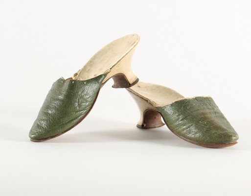 A pair of green leather mules, circa 1750-60, with: A pair of green leather mules, circa 1750-60, with white kid covered low curved heels, wide spoon-shaped insoles, the upper edged in white linen braid, 23cm, 9in long (2)