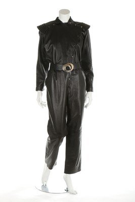 An early Thierry Mugler black leather jump-suit, late: An early Thierry Mugler black leather jump-suit, late 1970s, woven brown and gold label, the diagonal opening with popper fastening, quilted ribbed epaulettes, the leather belt with swirling gilt meta