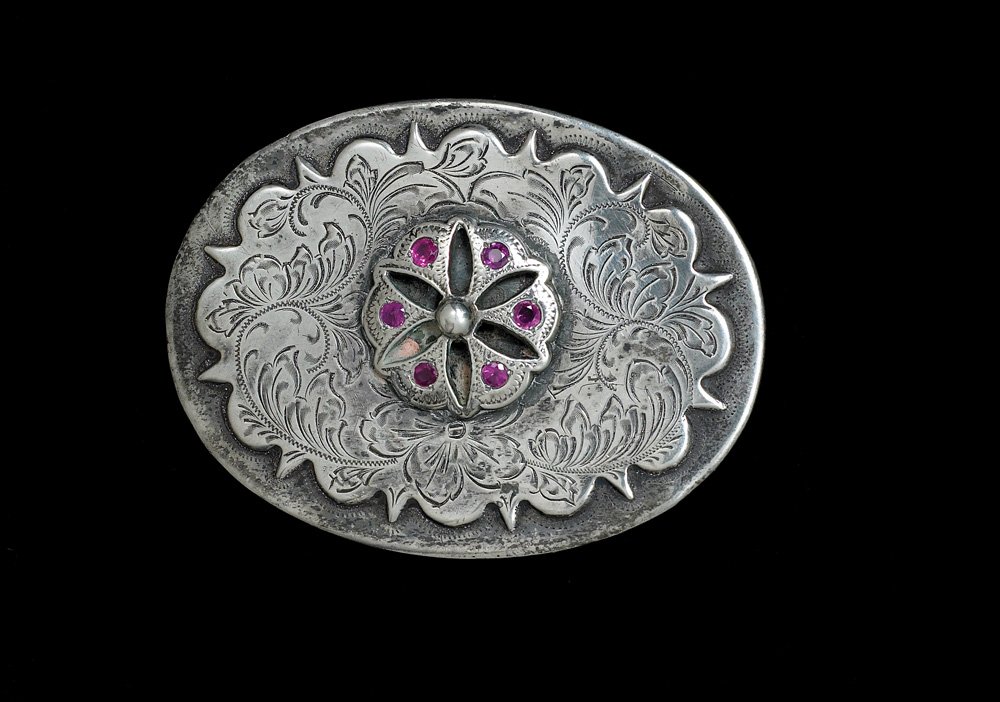 Sterling and Ruby Buckle: 3 1/2" x 2 5/8" oval shaped, finely engraved, with six rubies. Shows nice age and patina. Fine condition, c 1940s. PICTURED: Michael Friedman, Cowboy Culture, Pg 264. PROVENANCE: High Noon Collection
