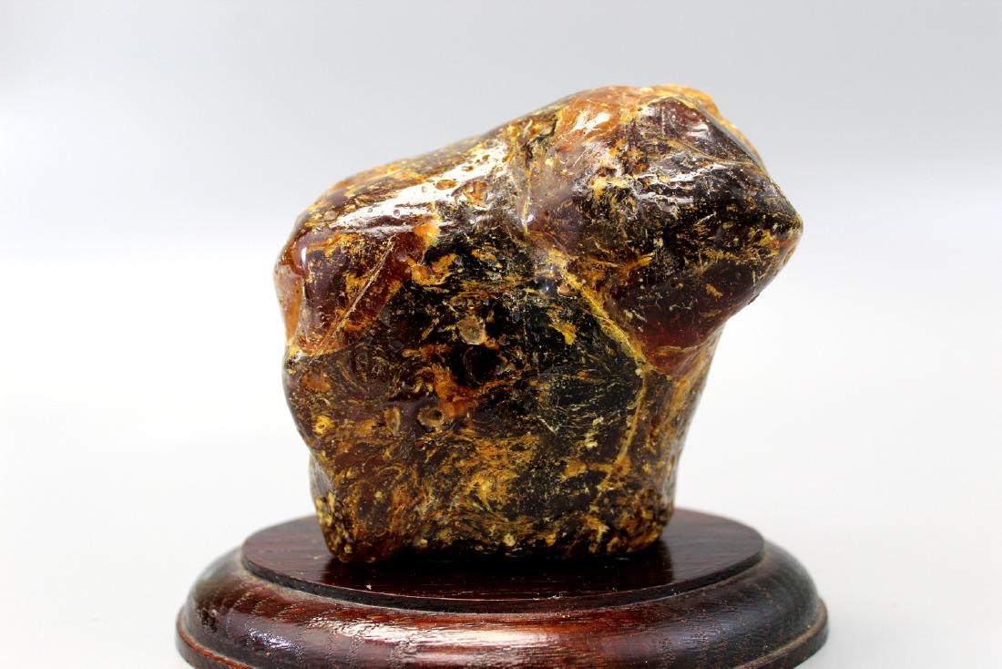 Large piece of amber on wood stand.: Large piece of amber on wood stand. Wt 385 grams. Length 13 cm. Width 10 cm.