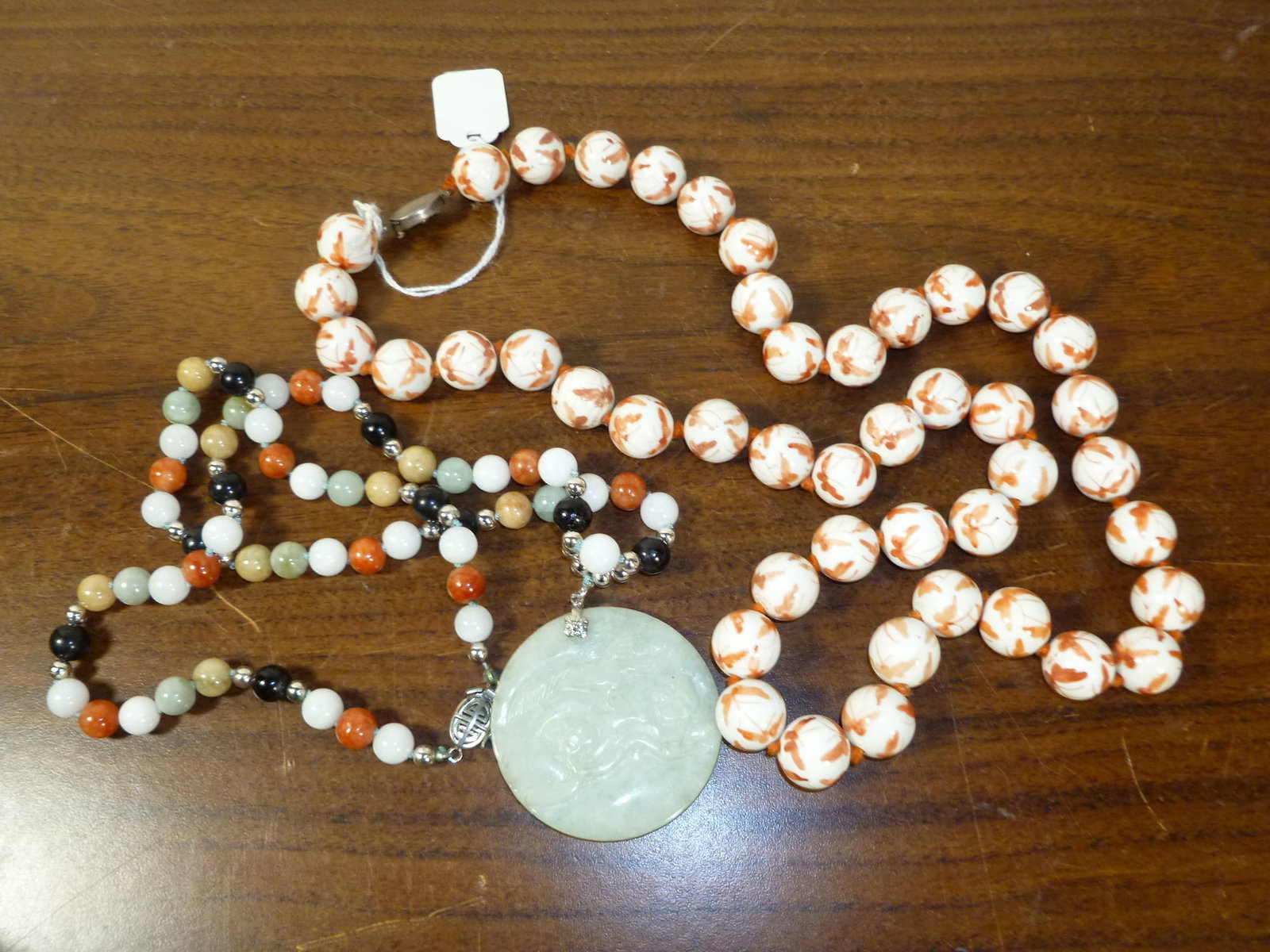 Two Asian necklaces, including one coral red porcelain beads with silver clasp and one jade stone: Two Asian necklaces, including one coral red porcelain beads with silver clasp and one jade stone beads . Porcelain bead diam 5/8". Length 28". Jade pendant diam 2".