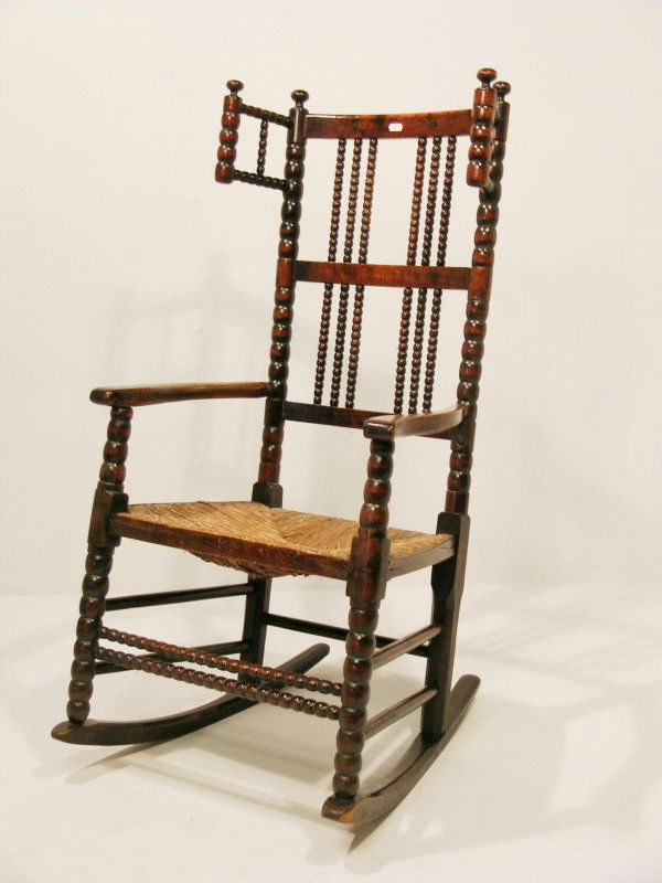 A bobbin turned rocking chair, 19th century, the: A bobbin turned rocking chair, 19th century, the winged back with turned finials, over shaped open arms and rush seat with side dust traps, above a bobbin turned double front stretcher and chamfered r