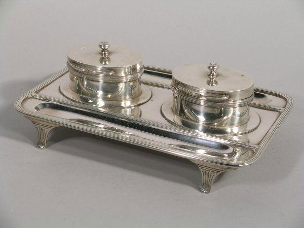 A silver inkstand, Charles Stuart Harris, London 1: A silver inkstand, Charles Stuart Harris, London 1894, of rounded oblong form with reeded rim, supporting two oval inkwells with clear glass liners and pen rests to either side, all raised on fan moul