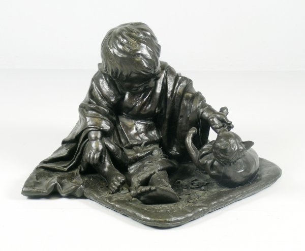 A cast bronze of a young boy seated playing with a