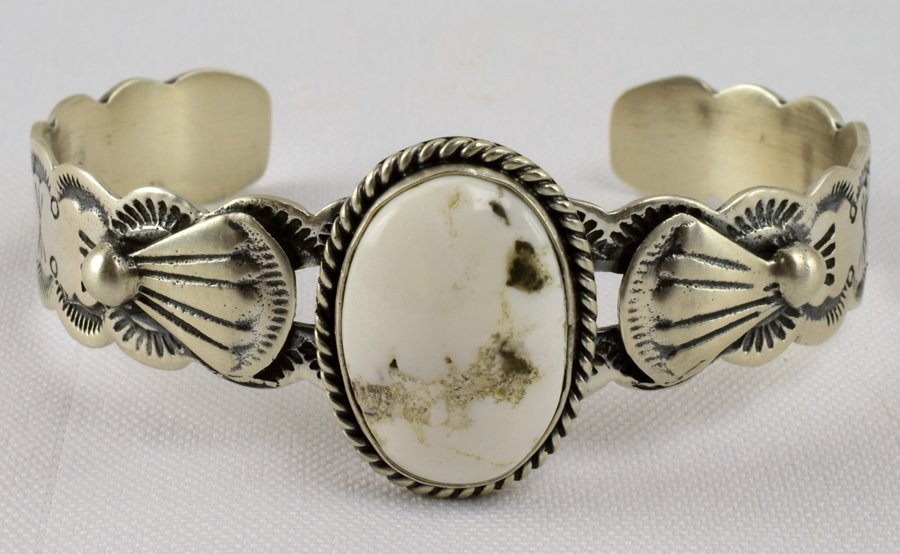 Lorenzo James Sterling White Buffalo Turquoise Bracelet: Measures 1 inch wide with a Natural White Buffalo Turquoise Center stone. The piece has a stamped scalloped band and Hand applied sterling design work. Inside measures 5.5 inches plus a gap of 1 inch.