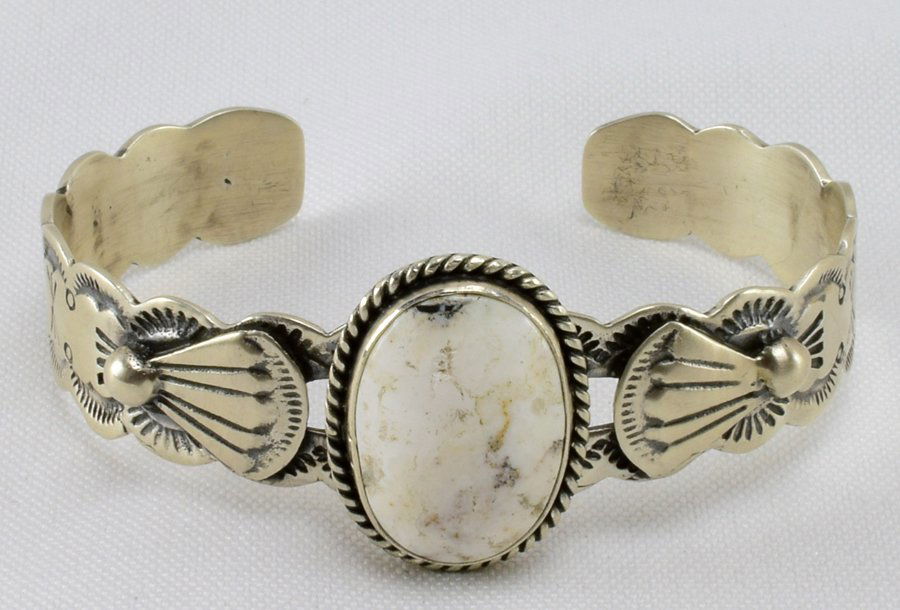Navajo, Lorenzo James White Buffalo Turquoise Cuff: Measures 1 inch wide in the center with an oval Cut Natural White Buffalo Turquoise center stone. The band is hand stamped and has applied detail designs. Inside measures 5.5 inches plus a gap of 1.25