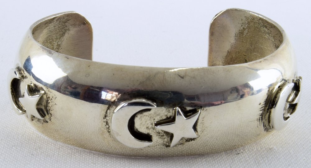 Russell Sam Sterling Silver Moon & Stars Cuff: Measure 7/8 inch wide in the center and flairs to 1 inch at the opening. This piece is done in Sterling Silver and is decorated with a raised Moon and Star symbol. Inside measures 5.75 inches plus a g