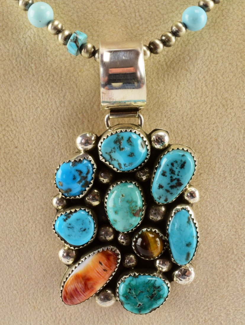 Navajo Kenneth Jones Sterling Kingman Turquoise Pendant: Measuring 2.75 inches from Bale to bottom x 1.5 inches wide. This pendant has Kingman Turquoise nuggets throughout and is accented with a Spiny Oyster piece and Tiger Eye Cabochon. Large round rain dr
