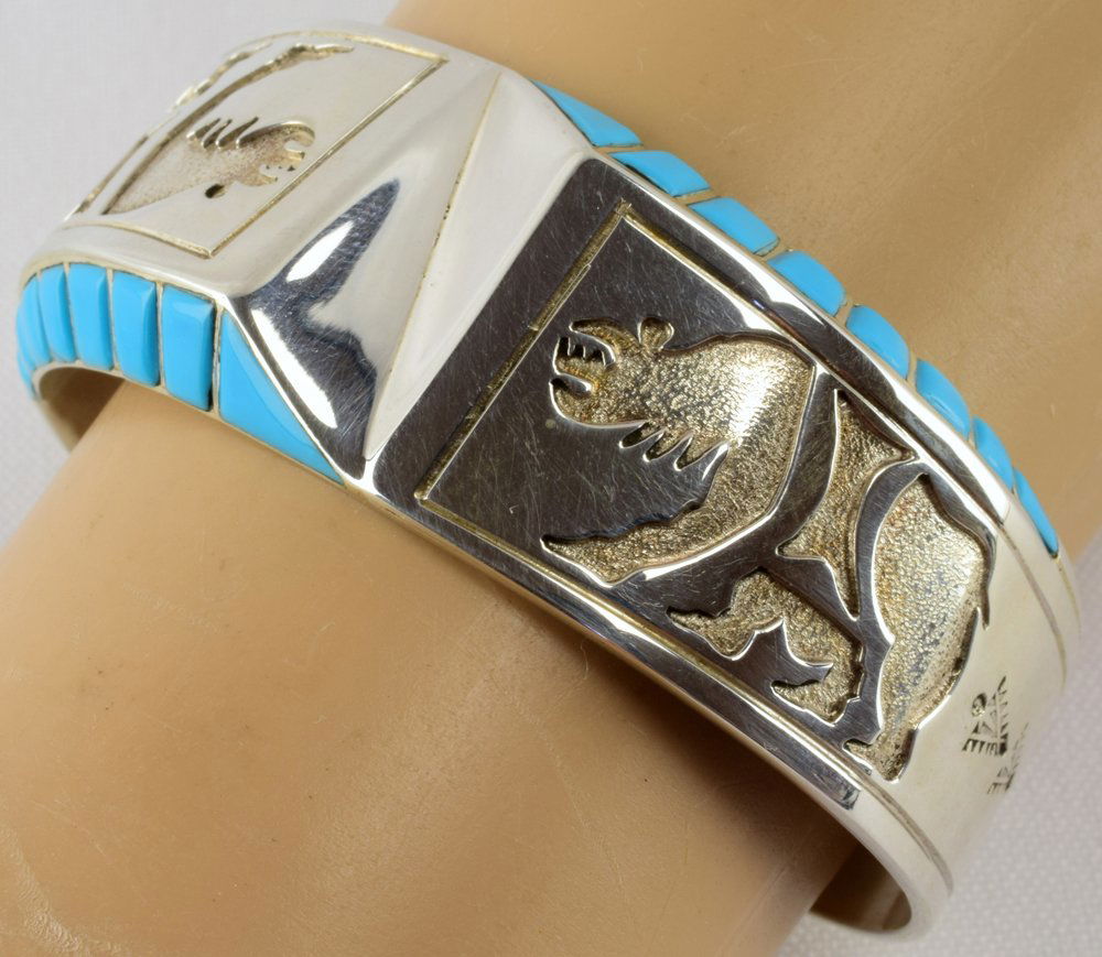Leonard Jim Sterling Petroglyph Bear Cuff W/Turq.: Measuring 1 inch wide in the center this piece is done in the artist's traditional style with a bear Pwtroglyph and hand inlay of Turquoise on the sides. Inside measures 5 3/8 inches plus a gap of 1 3