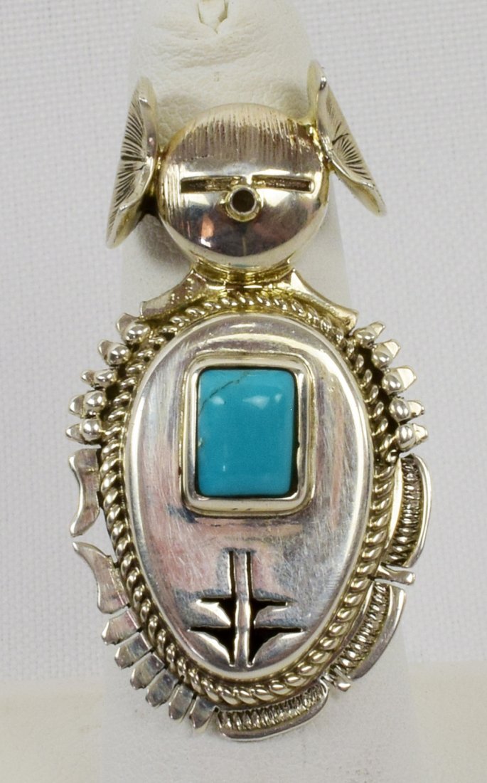 Bennie Ration Sterling Kachina & Turquoise Ring: Measuring 1.75 inches long this ring is made in a Kachina style with a Natural Turquoise Center stone. The piece has a Corn design on the front with beaded and rope accents. Stamped Sterling and Signe