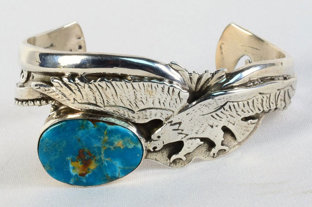 Robert Kelly Sterling Stormy Mtn. Eagle Bracelet: Measures 1.25 inches wide with a Large Stormy Mountain Turquoise Stone that has an American Eagle flying above. The band is highly decorated and the piece is heavy sterling. Inside measures 5.5 inches