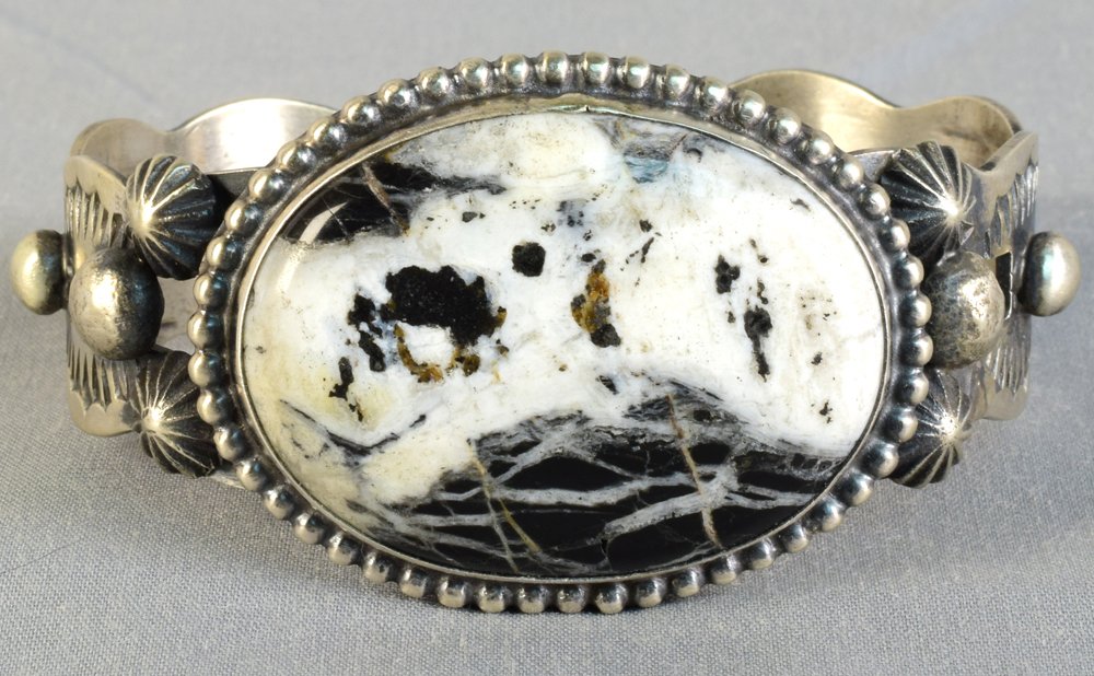 Navajo Sterling White Buffalo Turquoise Bracelet: Measures 1.5 inches wide with a White Buffalo Turquoise Center Stone that is set East to West. The stone is accented with a bead pattern and has a completely hand stamped band. The inside measures 6 i