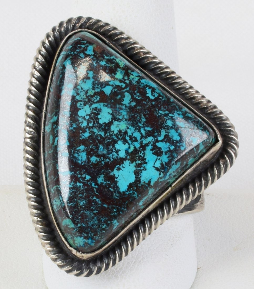 Native American Huebi Turquoise Men's Ring: Measuring 1.5 inches across this ring is done in a Free Form Style with a Huebi Turquoise Center Stone which is known for it's vibrant blue/green color. The ring is done in a Sand Cast Style. Stamped 