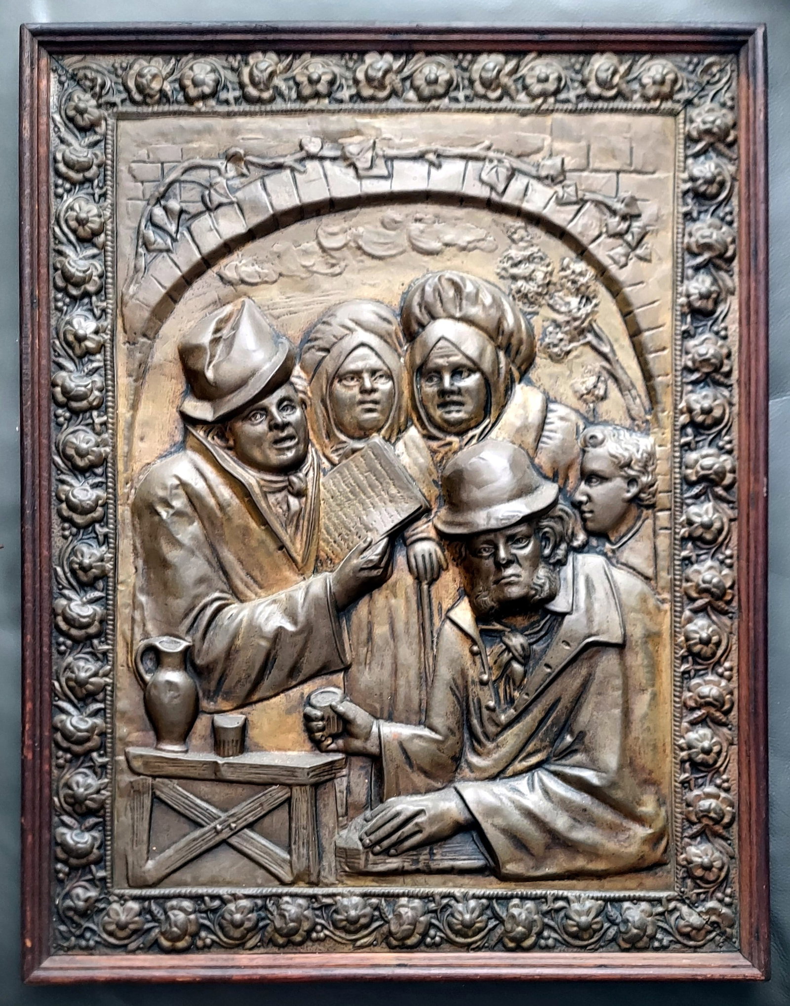 Victorian Metal Relief Shutter Panel, 19th Century: Victorian metal relief shutter panel depicting a group of reader and listeners, under an archway, with a detailed border featuring floral motifs. Sight 23 x 19, Wood frame 24 x 20 inches.