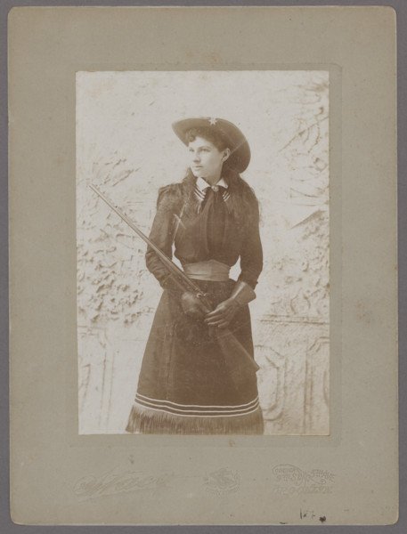 Three-quarter standing portrait of Annie Oakley: Shooting Star in High Fashion 467. [PHOTOGRAPHY]. [OAKLEY, ANNIE (sitter)]. STACY, Charles E. (photographer). Three-quarter
