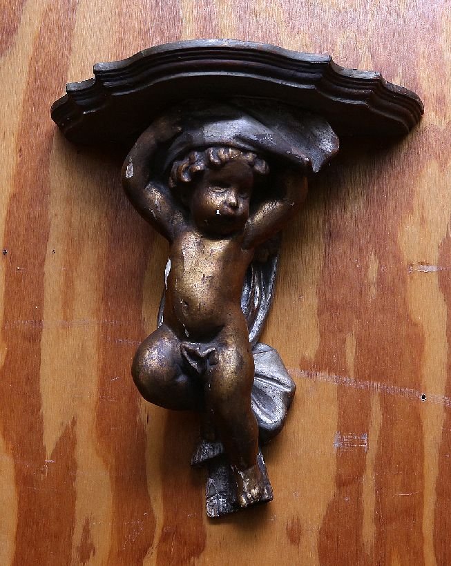 Pair of Carved Puti Brackets: Pair of 19th Century carved wood puti supporting scalloped shelves in a distressed gilt finish. Age: Last Quarter 19th Century. Condition: Good: Expected soiling and wear commensurate with age. Some c