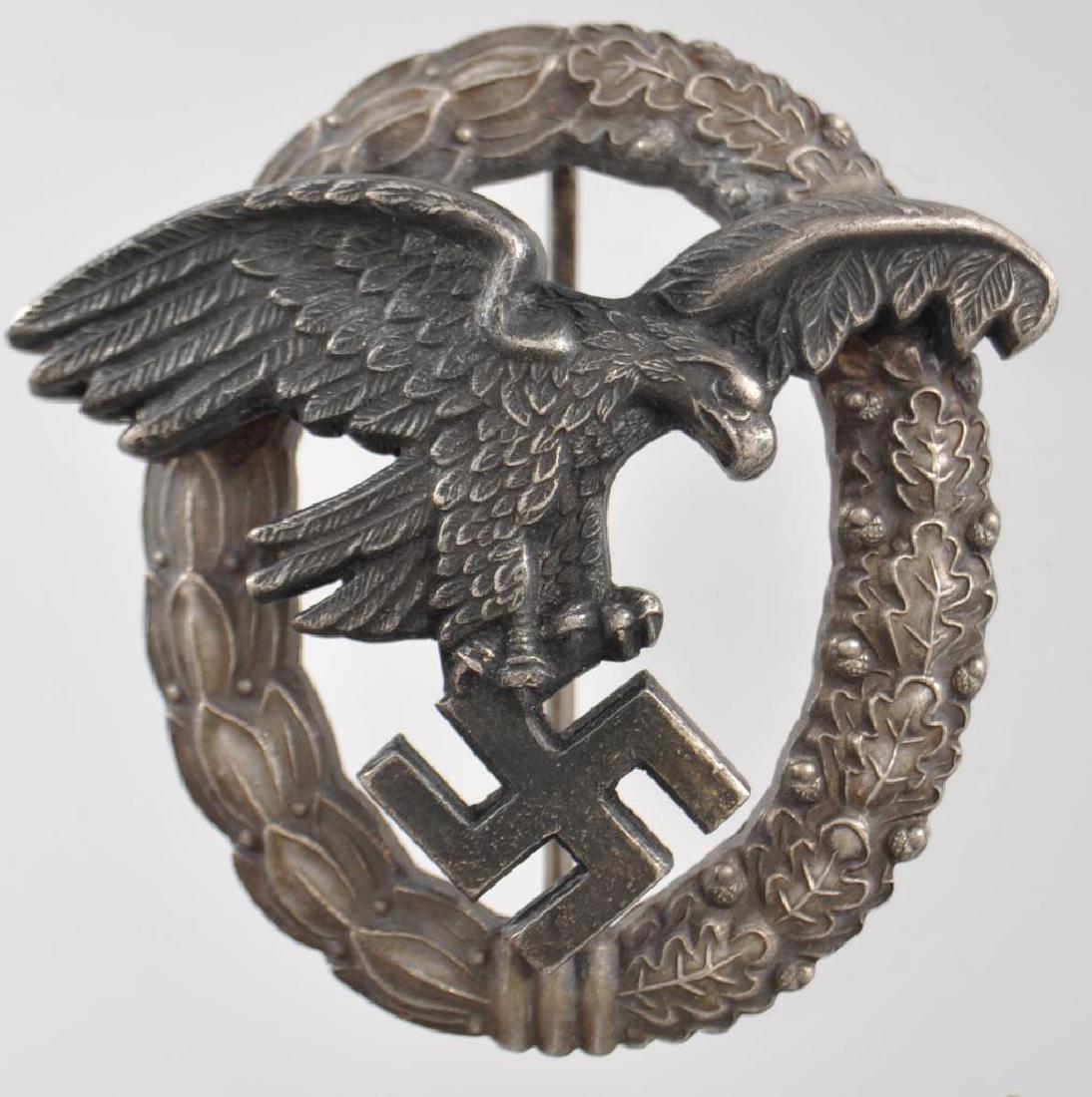 WW2 German Luftwaffe Observer Badge: The front shows a flying Luftwaffe eagle clutching a swastika in his talons. The reverse side of the wreath is maker marked A for the manufacturing firm of Assmann . Has a thin vertical T bar style pi