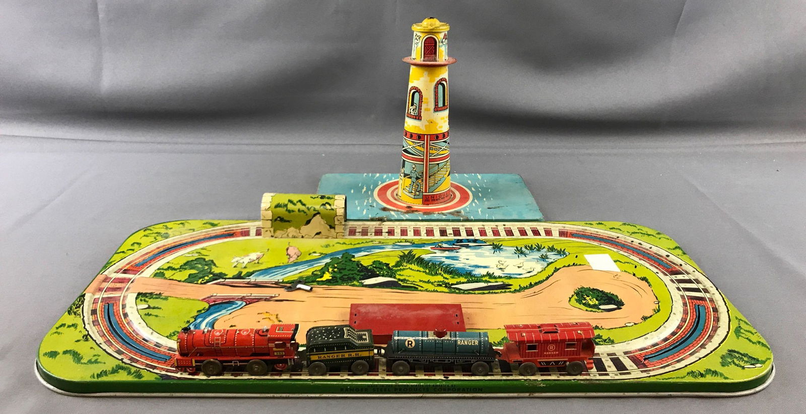 2 vintage metal toys, train and lighthouse: Ranger Steel Products Train Set is 21.5 inches by 11 inches, 4 cars and key. Unique Art Mfg Company lighthouse measures 8 inches tall base 10 inches by 5.5 inches. Both made in the U.S.A.