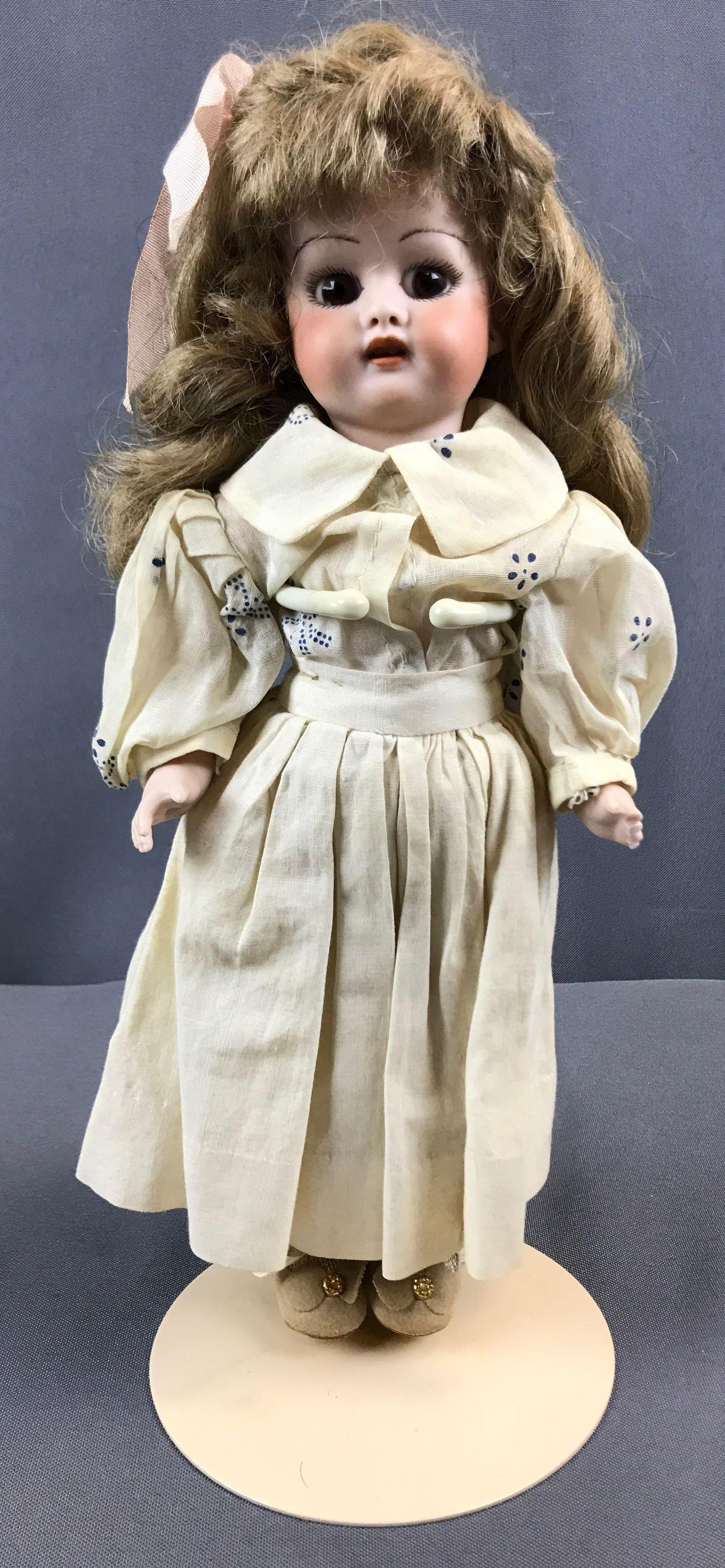 Antique Bisque Porcelain doll on stand: 11 inches tall, dark blonde hair, brown eyes. Fingers are broken on one hand. Wig is attached.
