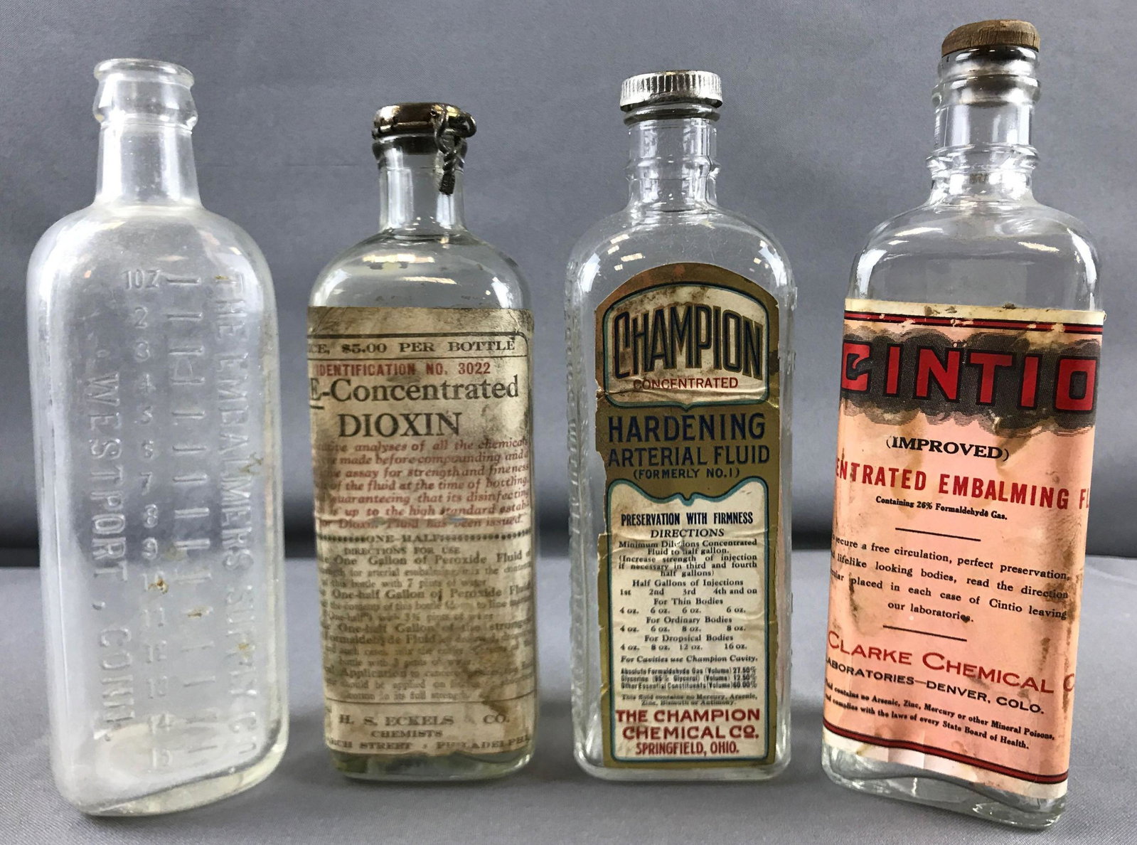 Group of 4 vintage embalming fluid glass bottles: 3 with lids and labels, tallest is 8.25 inches