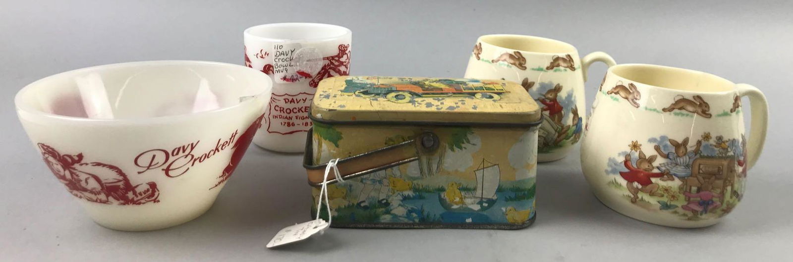 Group of 5 vintage childrens dishes and more: Fire King Davy Crockett bowl and Hazel Atlas mug, 2 ceramic Bunnykins mugs, and tin candy container. Largest is 4.75 inches. Tin container has flaking paint on lid.