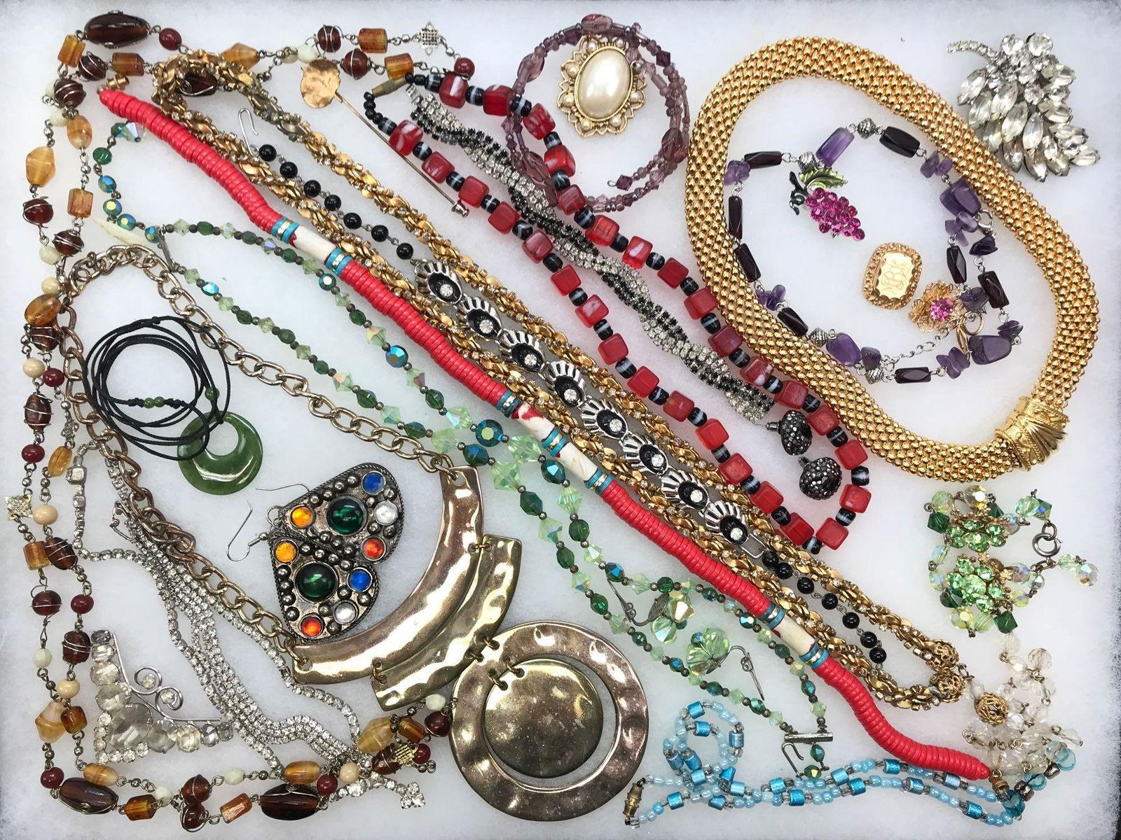 Day to Evening Costume Wardrobe: A vintage costume wardrobe that transitions from daytime to evening glamour showcases a variety of beaded chains, bracelets, and earrings. This choice lot features a sleekly stylized jade green pendan