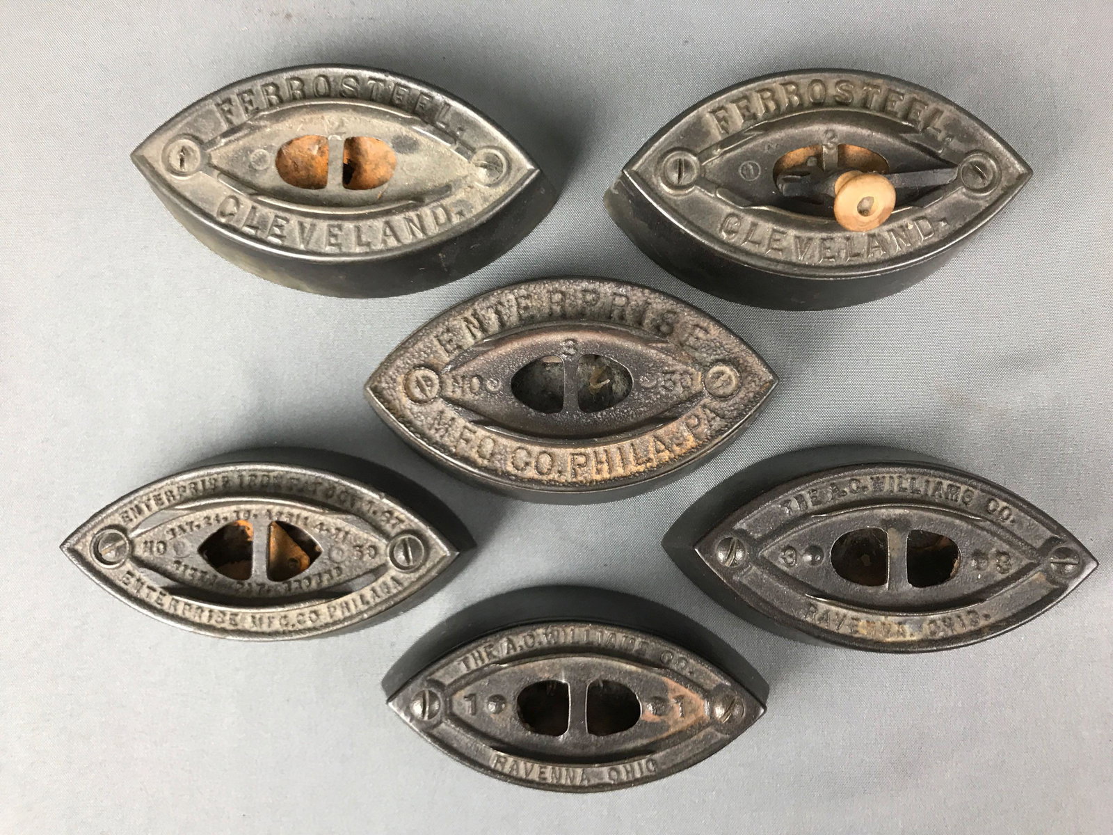 Group of 6 : Antique Sad Irons: Lot includes two sad irons marked "Ferrosteel, Cleveland" ; two sad irons marked "Enterprise, Phila".; and two sad irons marked "A.G. Williams, Ravenna OH". Largest is 6 3/4 inches in length