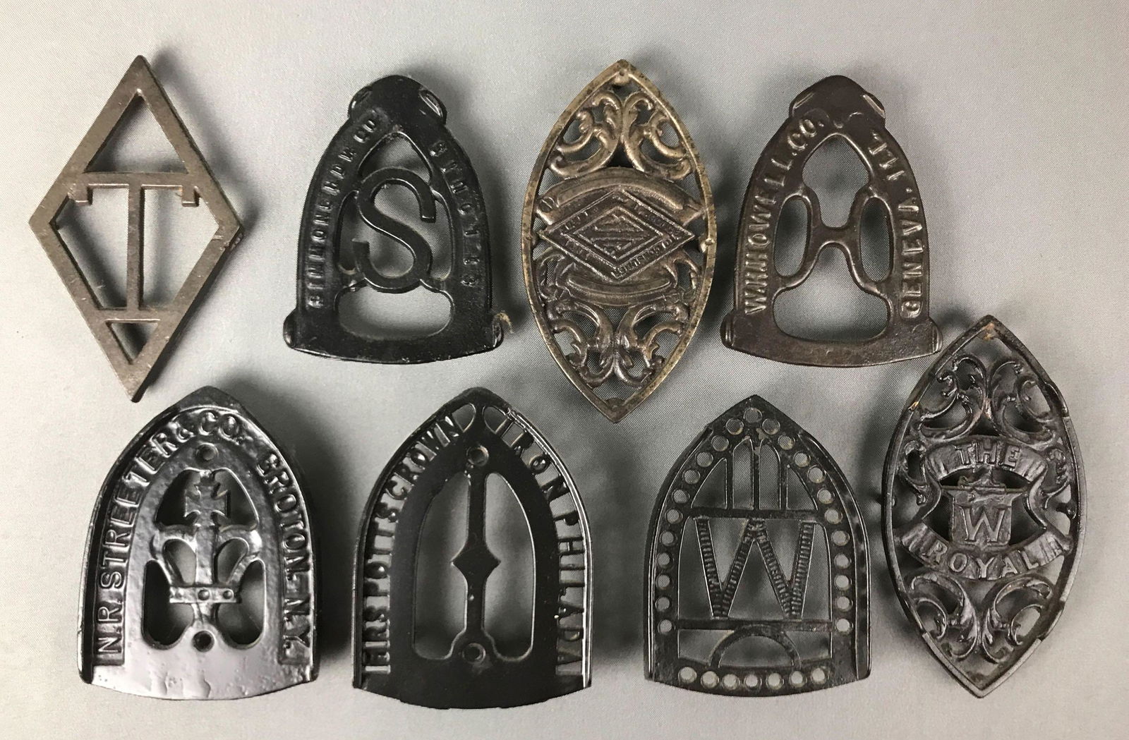 Group of 8 : Antique Cast Iron Sad Iron Trivets - Mrs.: The collection includes cast iron trivets marked "Mrs. Potts Crown", "W.H. Howell, Co."; "The W Royal"; "N.R. Streeter & co." and more. Longest measures 7 1/2 inches.