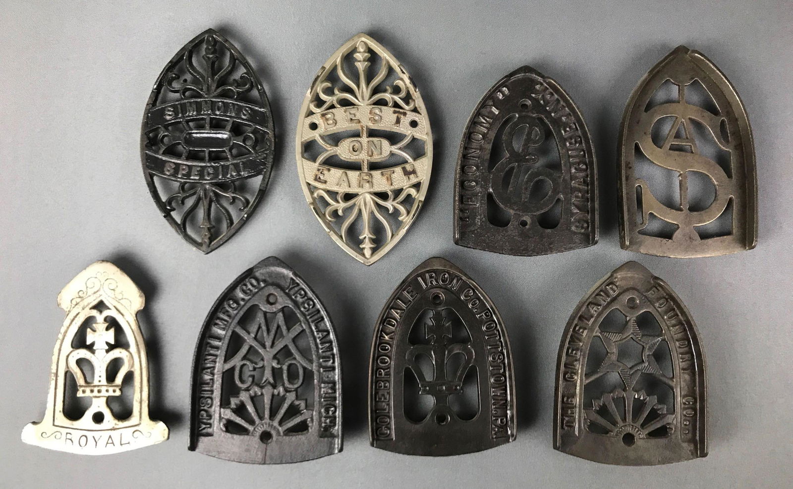 Group of 8 : Antique Cast Iron Sad Iron Trivets - "Best: This large collection of cast iron sad iron trivets includes : "Ypsilanti Mfg. Co."; " Simmons Special"; "Best on Earth"; "Royal" and more. One is cracked. Largest measures 7 inches