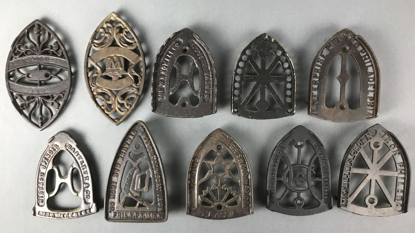 Group of 10 : Antique Cast Iron Sad Iron Trivets -: Collection includes trivets marked "Griswold, Erie PA"; "Enterprise", "Hibbard Spencer"; "Mrs. Potts Crown" and others. Largest is 7 1/2 inches in length