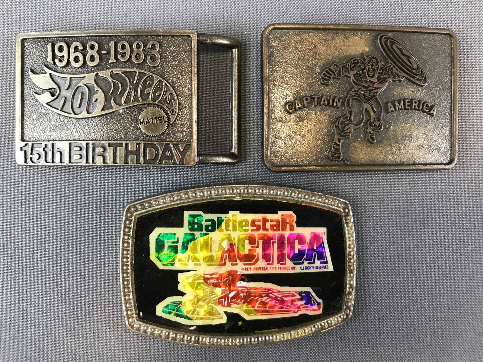 Group of 3 Licensed Metal Belt Buckles: Captain America, Hot Wheels 15th Birthday, and Battlestar Galactica. Largest is 3.5x2.5 inches