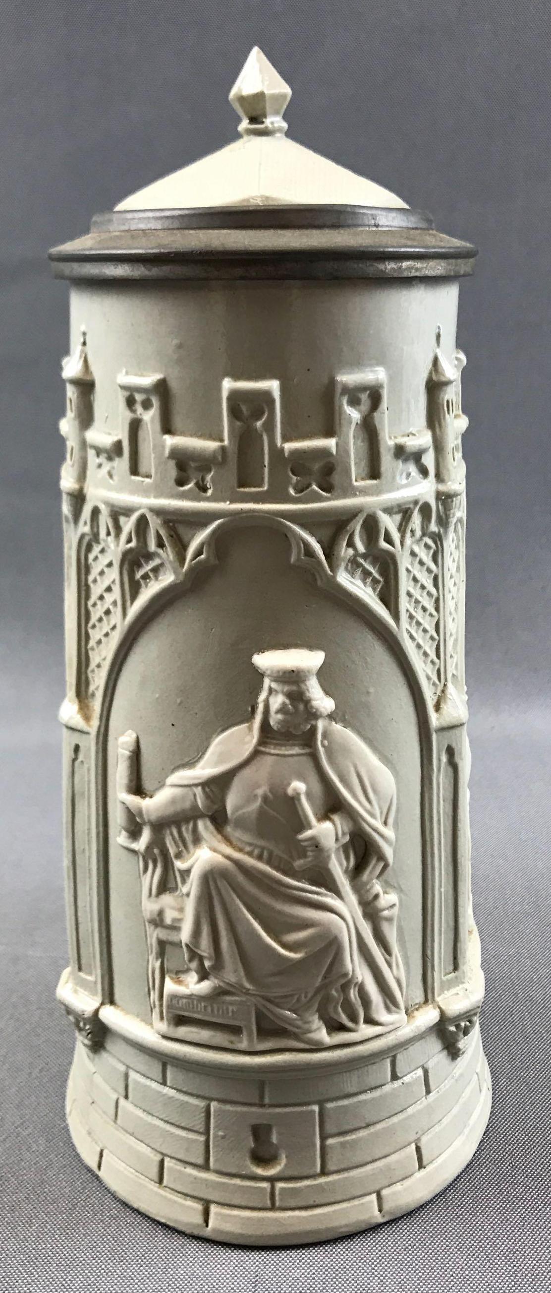 Vintage Bas Relief Stoneware Stein: 9 inches tall; stein features a bas relief tableau of a king and his drinking associates within this unique castle-shaped lidded stoneware stein - stamped "32" on the bottom