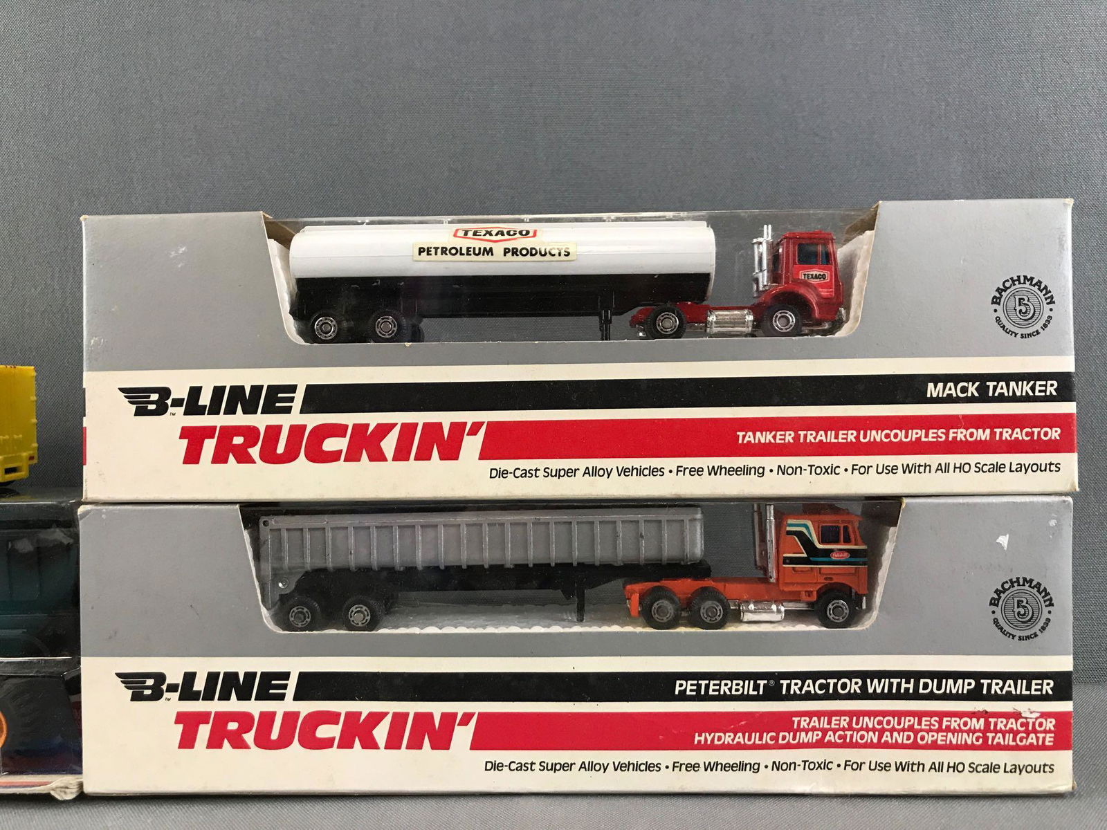 Group of 4 assorted die-cast metal and plastic: Bachmann HO scale Mack Tanker and Peterbilt Tractor with dump trailer in original packaging, Hot Wheels Thunder Roller Mayflower 1:64 scale, and Top Trucks Dump Trailer