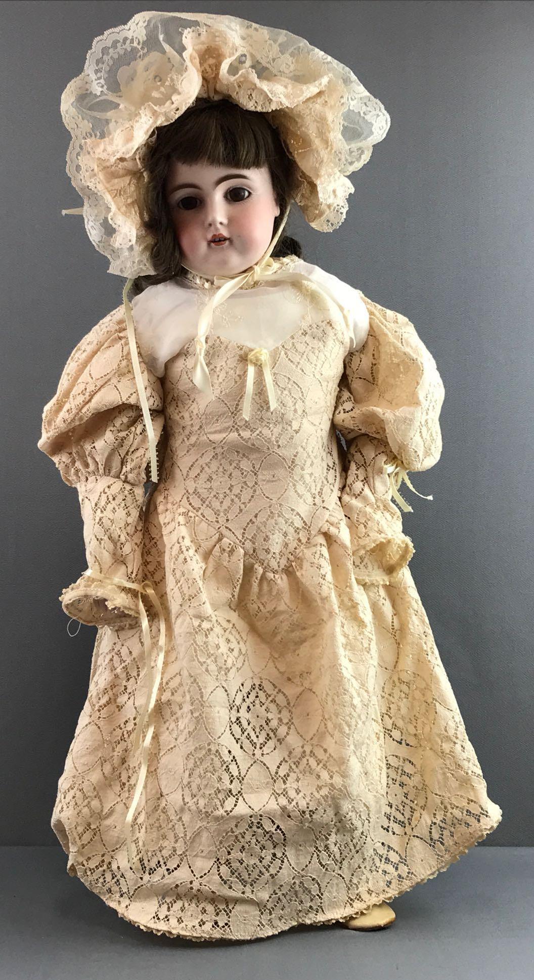 Antique 27 inch German bisque doll Kestner: Back of head reads 15, 147. Shoulder head, brown sleep eyes with painted lashes, open mouth with teeth, leather body, bisque arms. Body has repairs. Brown hair wig, attached. Cream lace dress, bonnet.