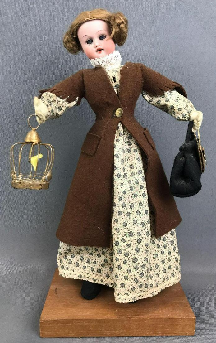 Vintage 12 inch bisque doll on stand: Made in Germany, Herm Steiner, 14/0. Socket head, blue sleep eyes with painted lashes, open mouth with teeth, fabric wired body. Felt coat, floral dress, with bags, birdcage. Brown mohair wig, unattac