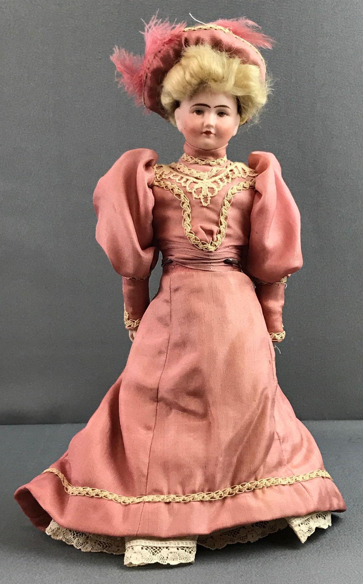 Vintage Verlingue bisque doll: Measures 11 inches tall. Back of head reads Lutin France, JV anchor symbol 3/0. Gibson girl with mauve pink dress and hat, mohair blonde wig, attached. Doll stand not included.