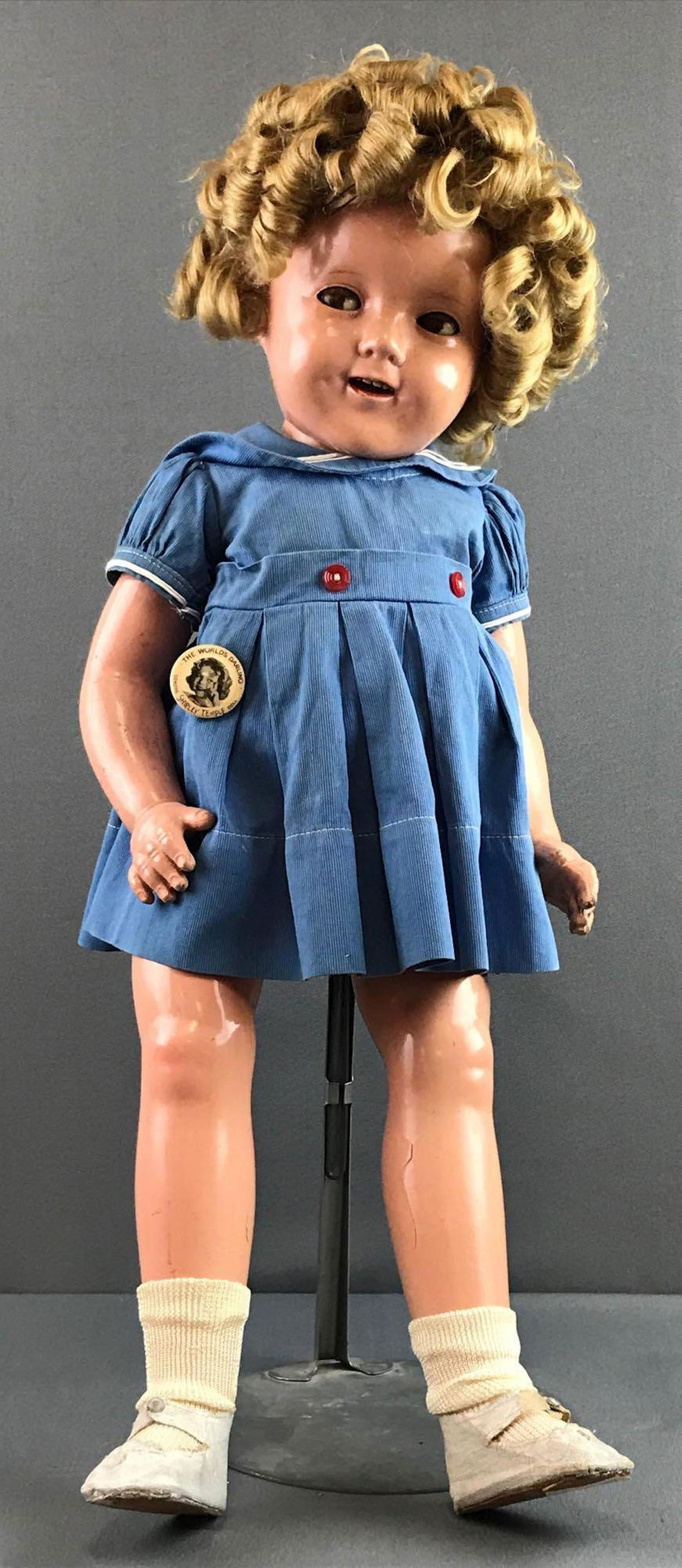 Vintage Ideal Shirley Temple doll: Measures 25 inches. Mohair wig, attached. Composition. Head and body marked Shirley Temple. Eyes move side to side. Eyes, body, finish all show wear, chipping, cracks. Some discoloration to face. Incl