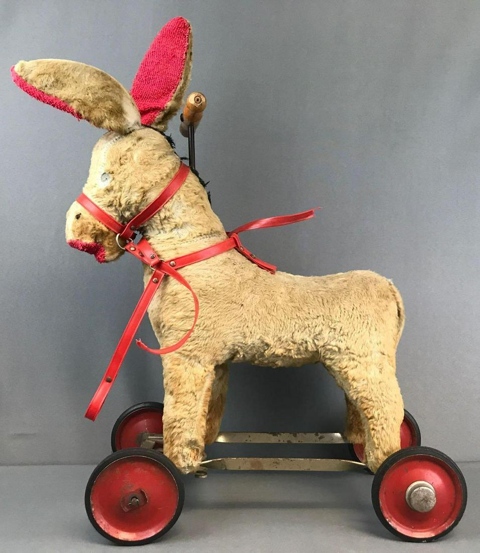 Antique ride-on donkey: Straw stuffed mohair, metal frame and wheels. Well loved, signs of repair, missing eye, broken harness. 19.5x9.25x25 inches