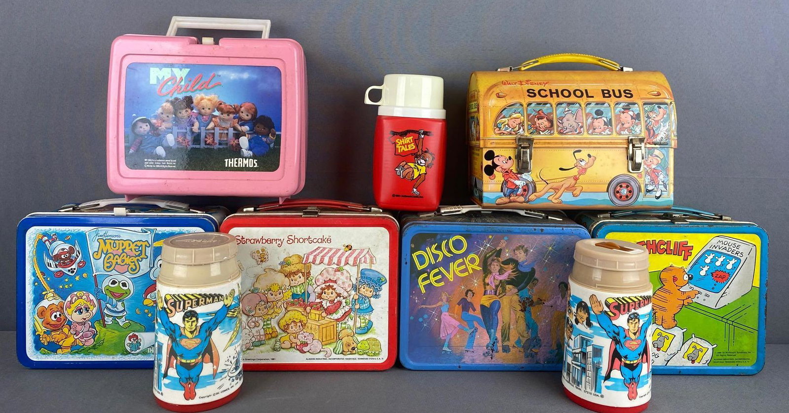 11 piece group of lunch boxes, thermoses: Metal, plastic. Muppet Babies and Strawberry Shortcake include matching thermoses. Some rust, discoloration